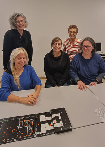Photo de groupe de 5 femmes réunies autour d'une table avec des plans tactiles Virtuoz étalés. Elles sourient, symbolisant la coconstruction d’un projet d’accessibilité.